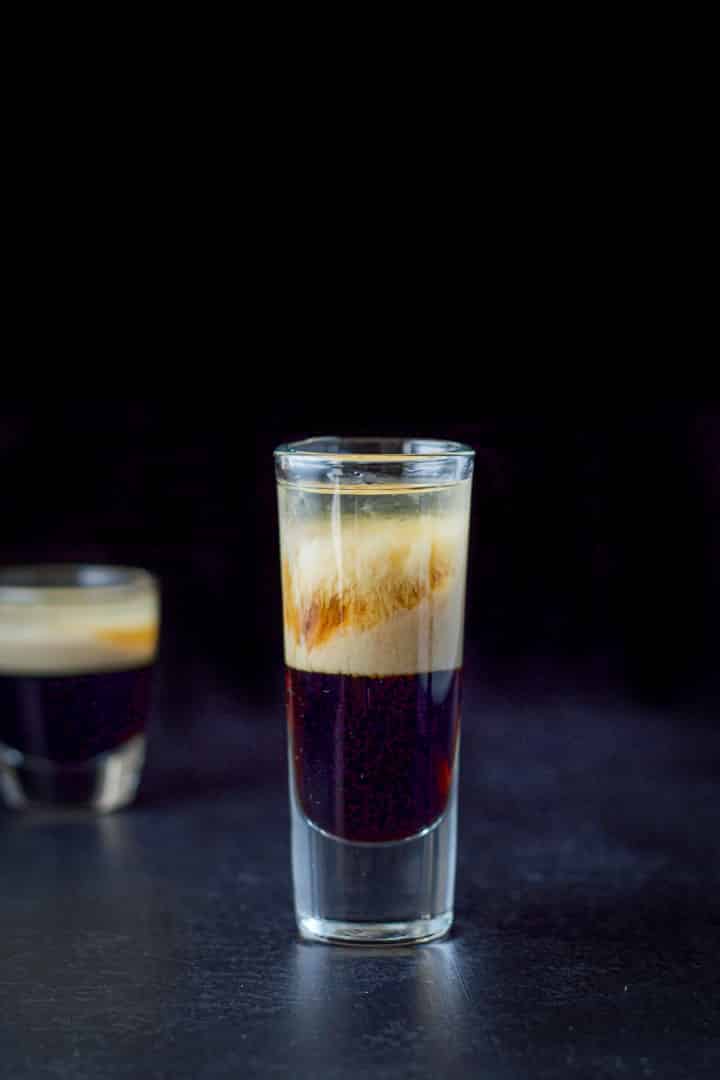 The tall glass showing the infiltration of two of the ingredients and there is also a shorter glass in the background