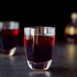 Vertical view of the layered raspberry kiss shot in the two glasses with the small chambord in the background - square