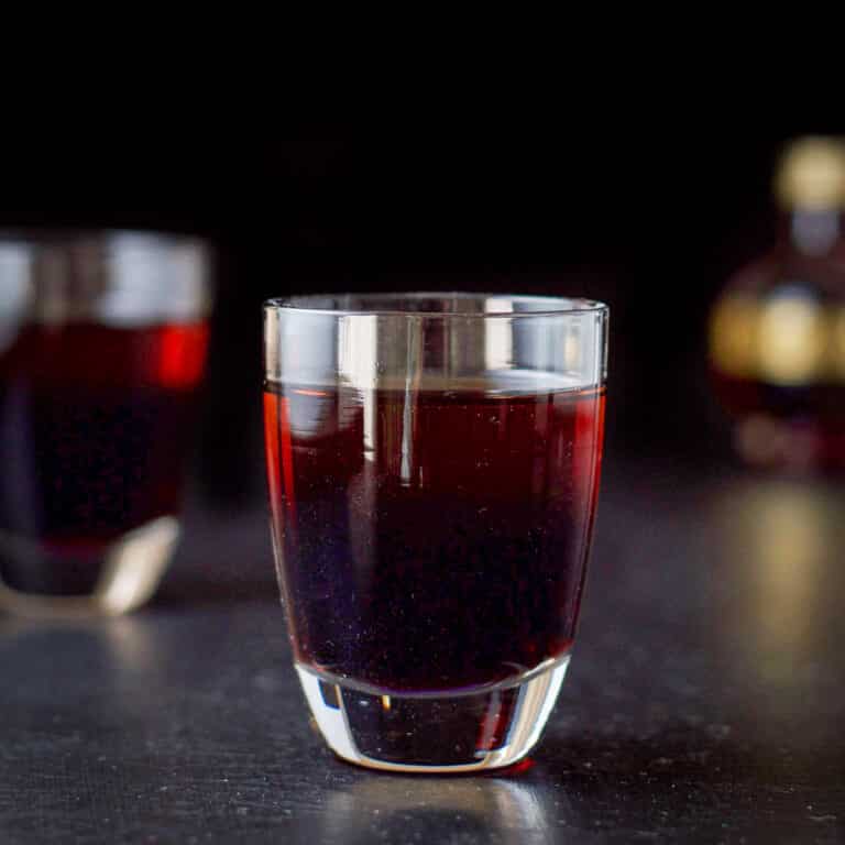 Vertical view of the layered raspberry kiss shot in the two glasses with the small chambord in the background - square