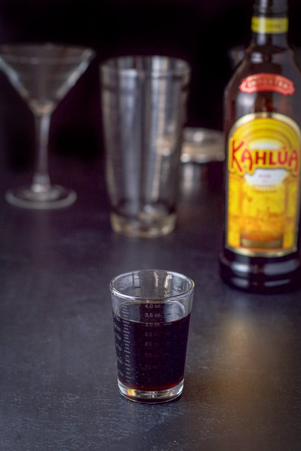Kahlúa poured out with the bottle in the background along with the shaker and glass