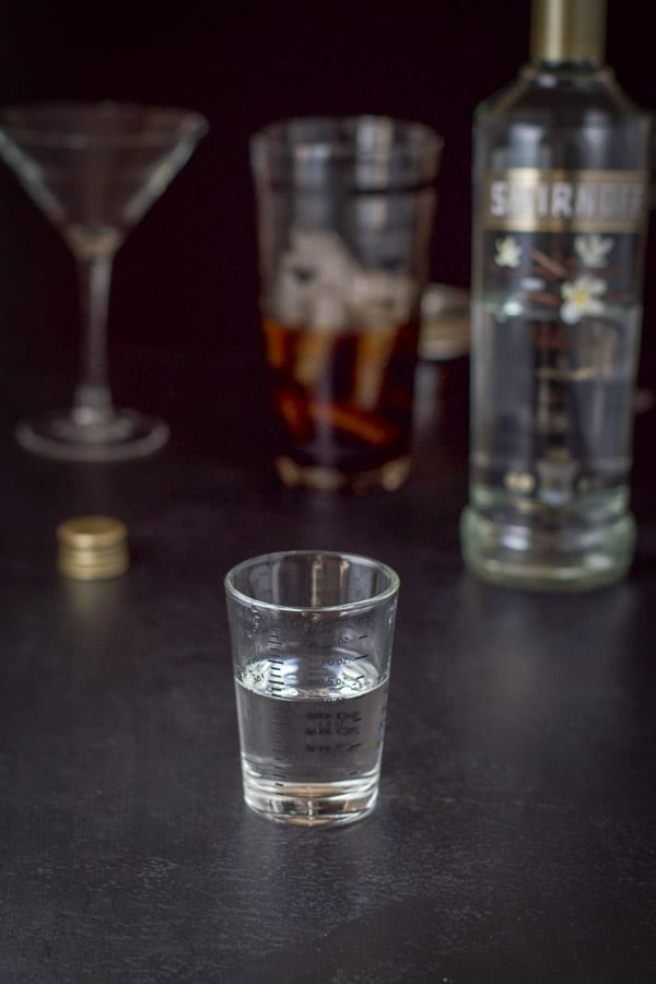 Vanilla vodka poured out with the bottle, shaker and glass in the background