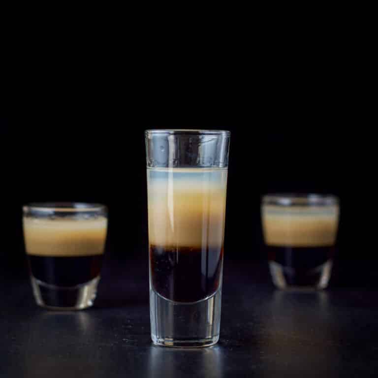 Vertical view of the tall glass filled with the peppermint shot with two other glasses behind it - square