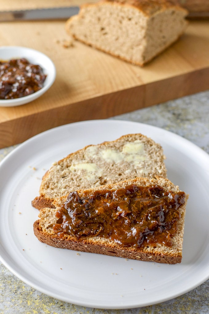 A white round plate with two pieces of bread on it, one with spread and the other with butter