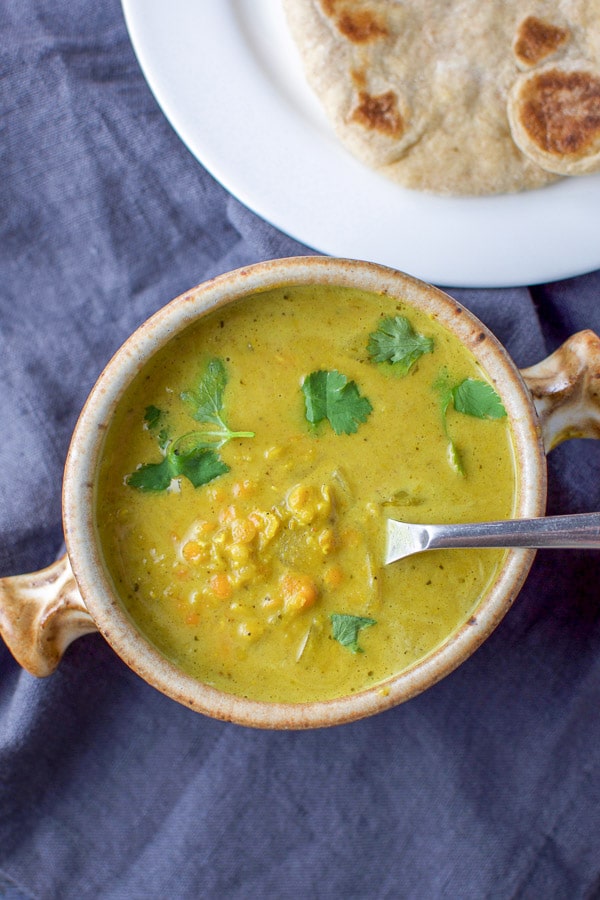 Overhead view of the coconut lentil soup in a crock with a spoon in it and some naan in the background