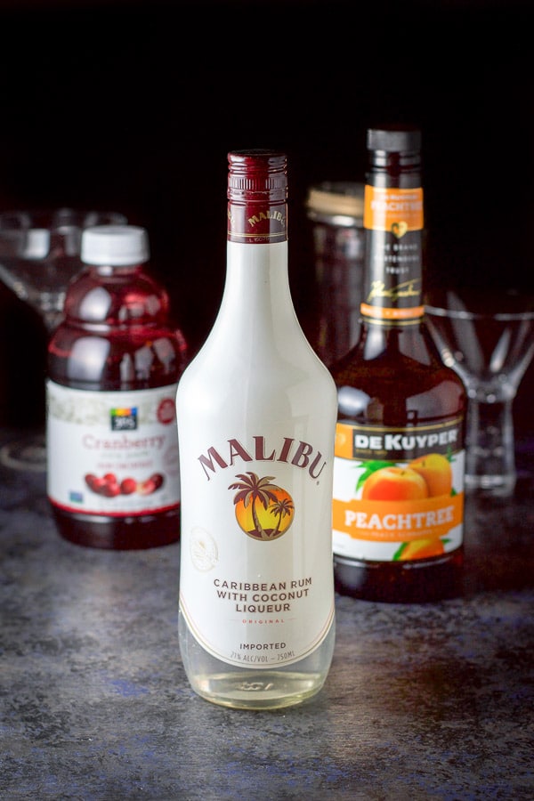 Coconut rum, peach schnapps and cranberry juice with some glasses and a cocktail shaker in the background