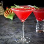 A classic martini glass in front of the bubble glass filled with the pomegranate cocktail - square