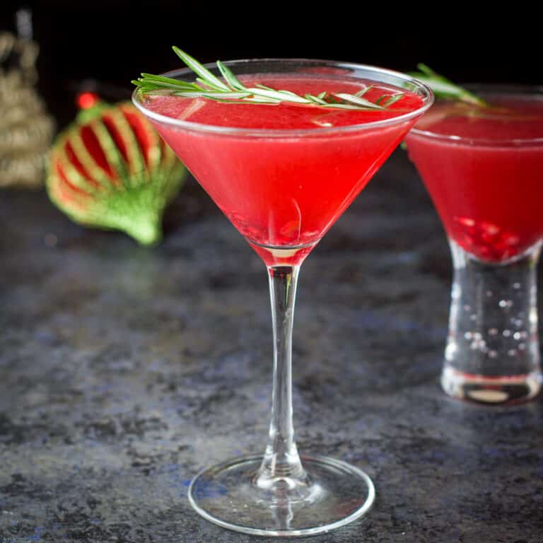 A classic martini glass in front of the bubble glass filled with the pomegranate cocktail - square