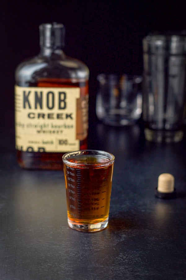 Bourbon measured with the bottle, glass and shaker in the background