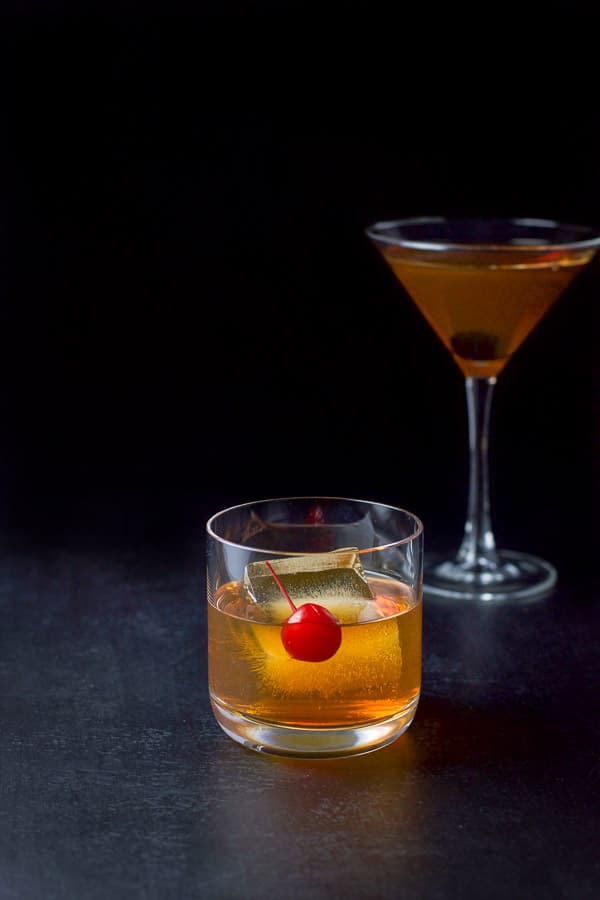 The bourbon drink in a rocks glass and martini glass with cherries as garnish