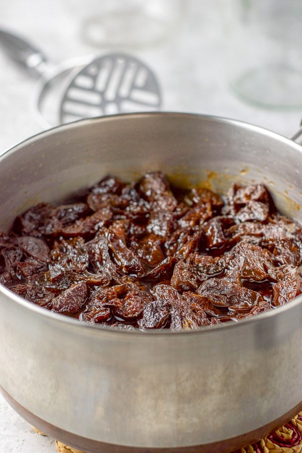 Prunes are done and plump in the pan and there is a potato masher in the background