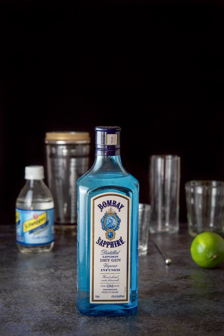Gin, lime and club soda on the table with the shaker, glassware and a measuring glass