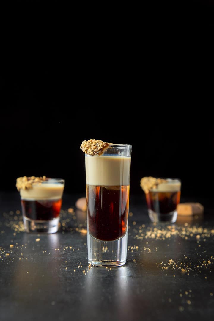 Tall glass filled with layered shot in front with candy garnishing the glass and candy bars on the table