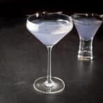 Curved glass of the purple cocktail in front of the bubble glass with the cocktail - square