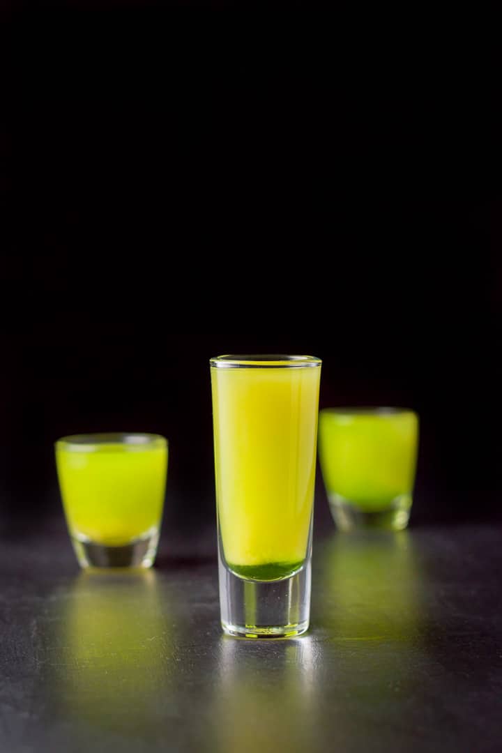 Vertical view of the tall glass filled with the layered shot with the other two glasses in the back