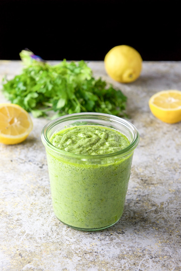 Closer view of the avocado spread in a jar with some lemons and herb in the background