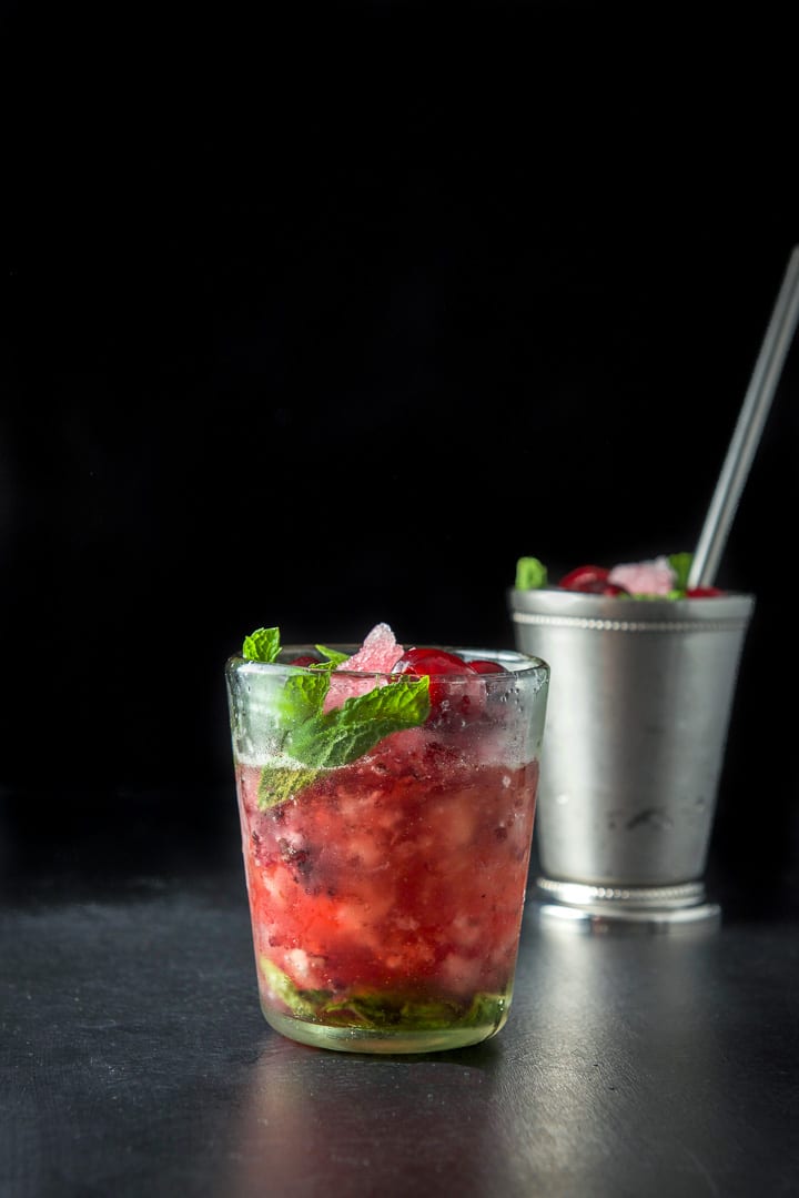 Glass filled with the cherry and mint cocktail with the metal glass and straw in the background