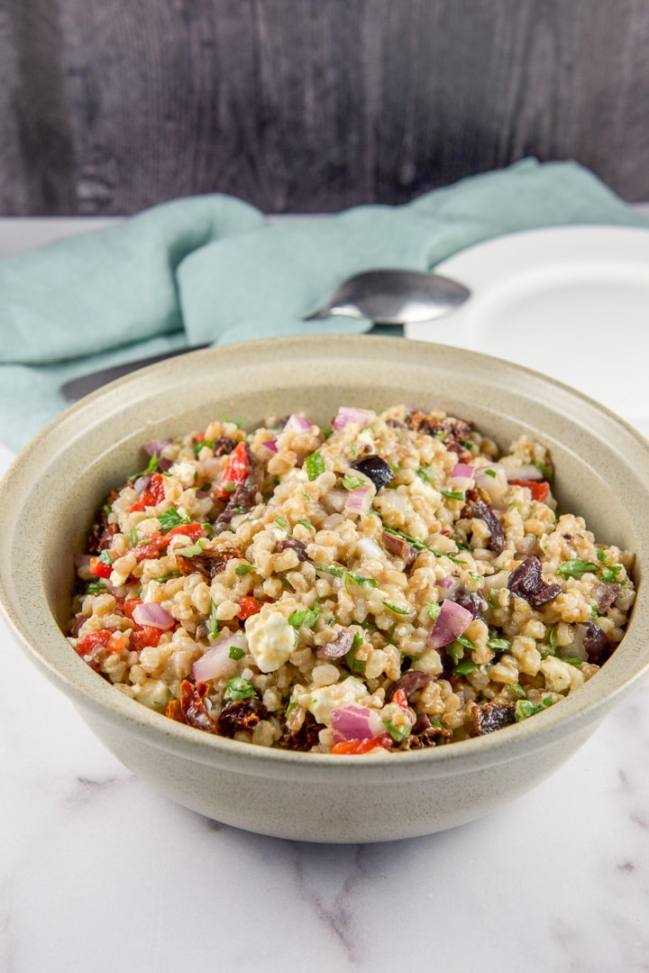 Closer look for the salad in a beige bowl with a plate, spoon and napkin behind it