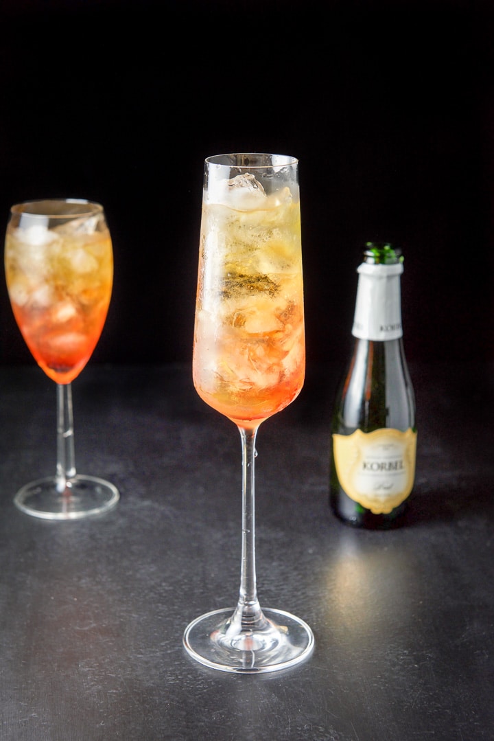All the ingredients except the champagne in the two glasses with ice and the bottle in the background