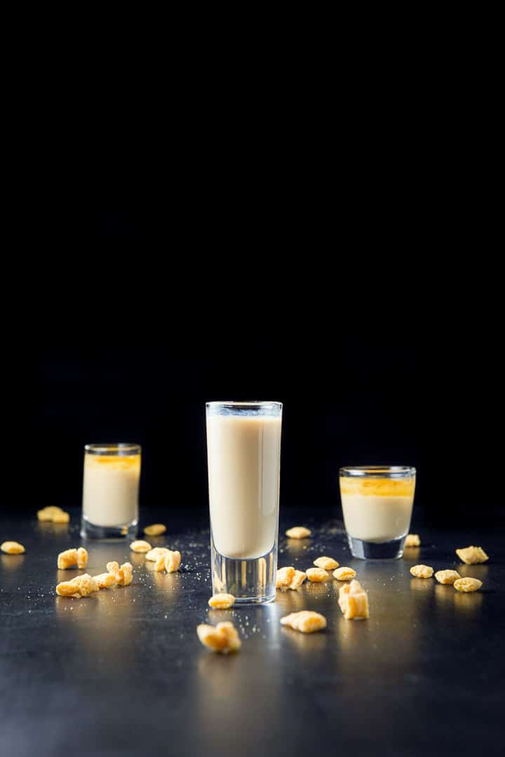 Vertical view of the tall glass filled with the mixed shot with the two layered ones and cereal in the background