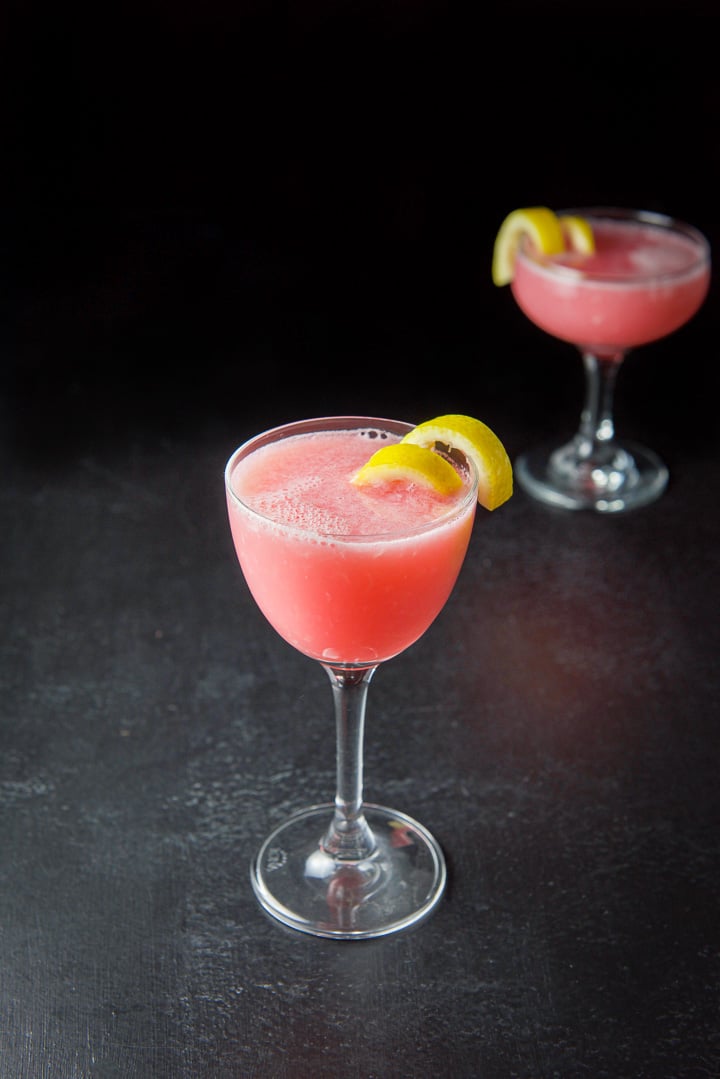 Tall martini glass in front filled with the cocktail with lemon twists as garnish