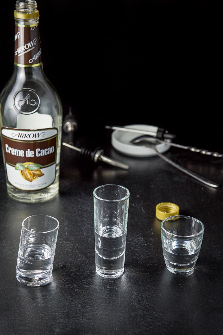Creme de cacao poured in the three glasses with the bottle, spoon, pourer and eye dropper in the background