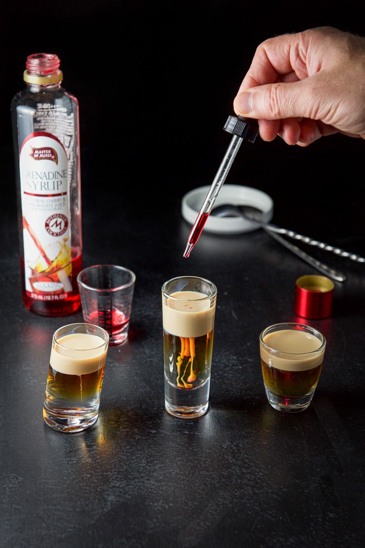 A hand with a dropper dropping a few drops of grenadine in the three glasses