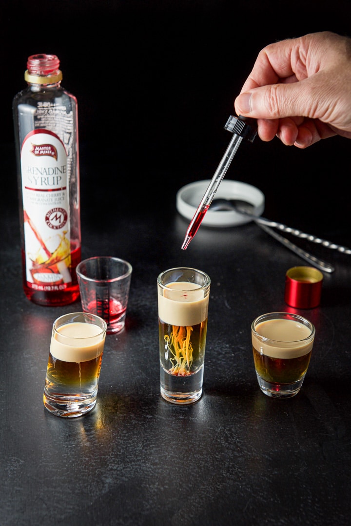 A hand with a dropper putting more drops of grenadine in the shot