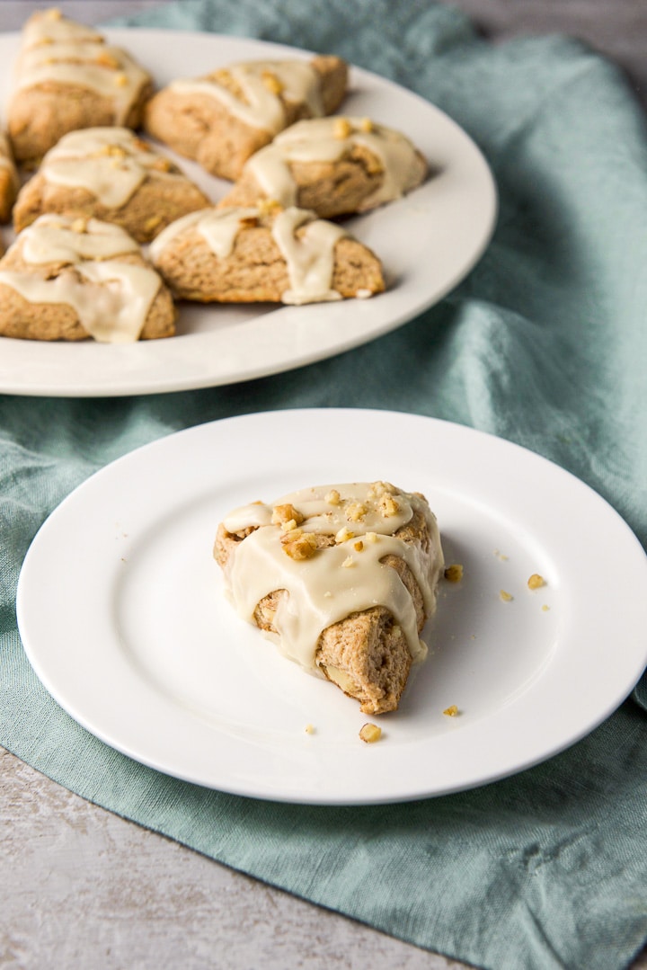 One of the glazed scones on a white plate with a bigger plate in the background with more scones