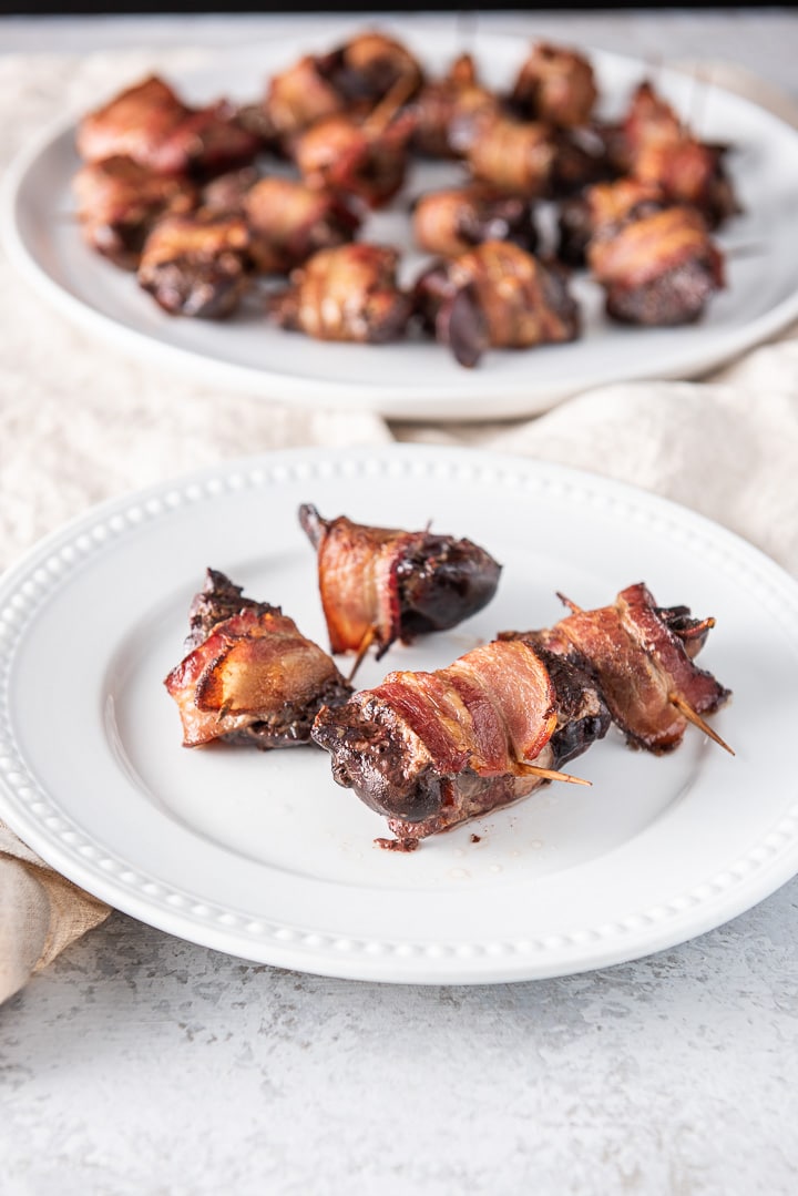 A small plate of livers wrapped in bacon in the foreground with a big plate in the background