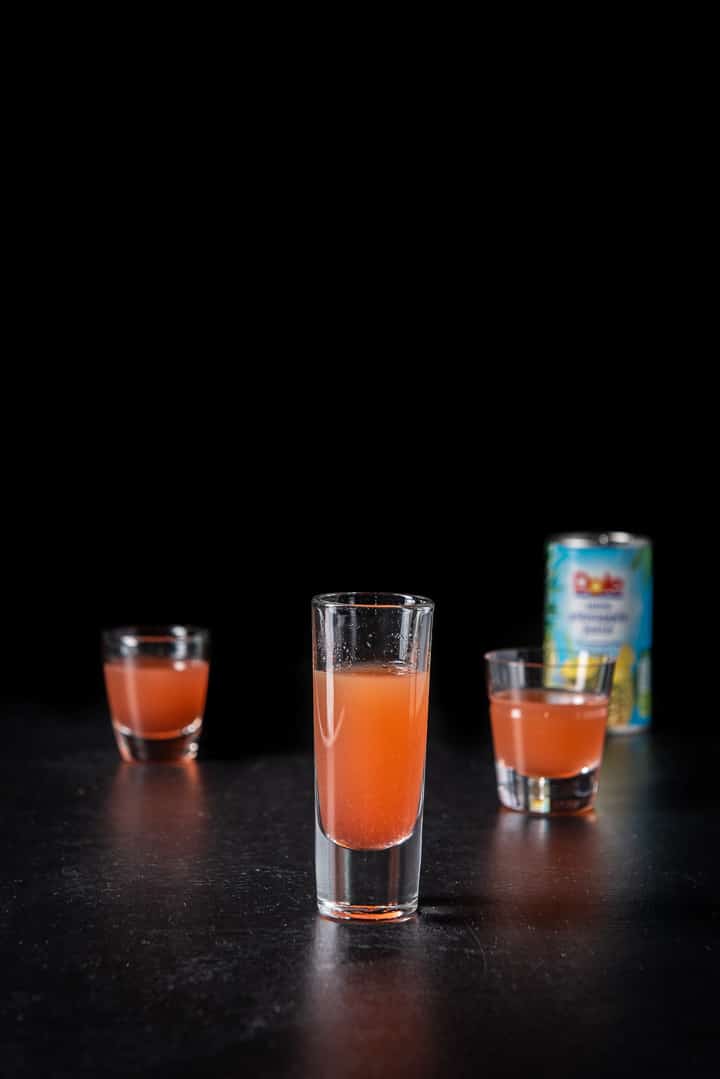 Pineapple juice poured in the shot glasses with the pineapple juice in the background