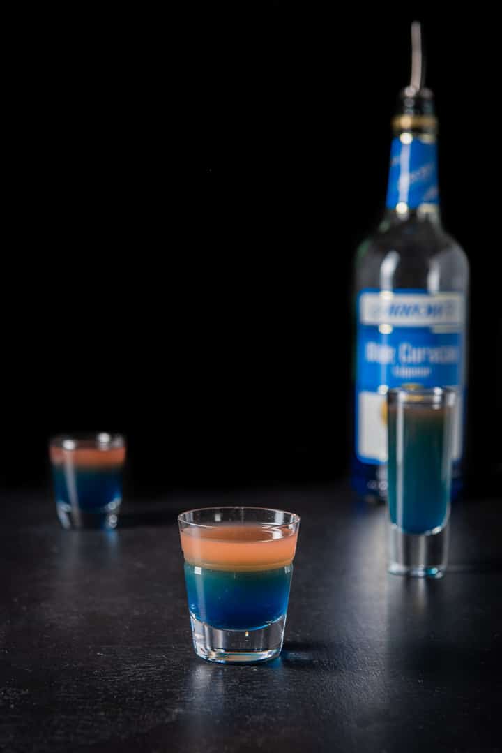 Blue curacao poured into the beveled glass with the layers clear, there is the bottle in the background
