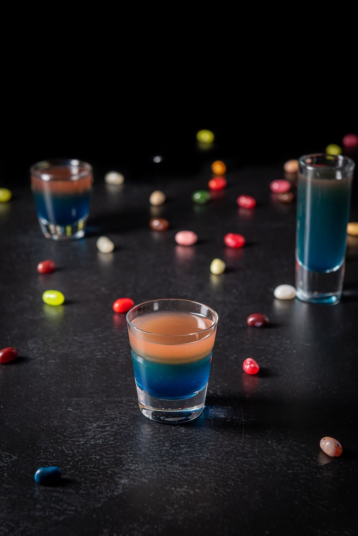 Higher view of the beveled glass filled with the shot with the other glasses and jelly beans in the background