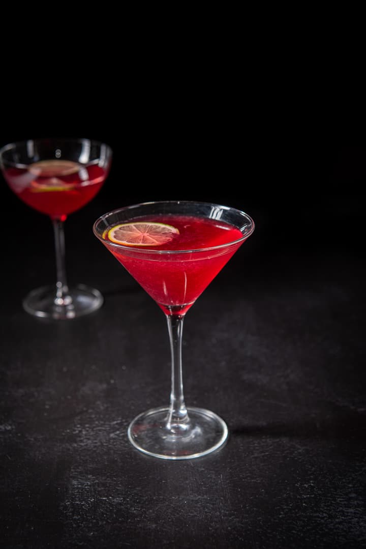Pomegranate cocktail in the classic martini glass in front of the bowl glass filled with the red cocktail