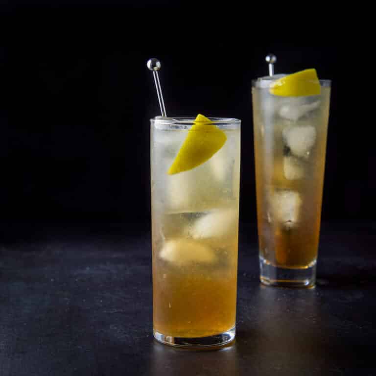 Collins glass with the amber cocktail in front of the wider taller glass - square