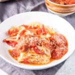 Square photo of the deep white plate with lasagna with red sauce and cheese sprinkled on it