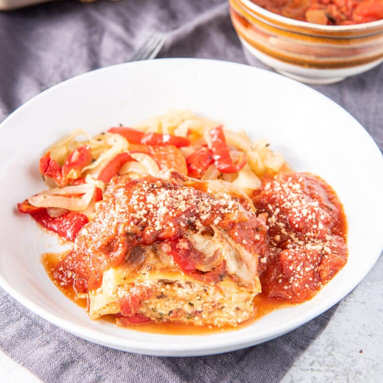 Square photo of the deep white plate with lasagna with red sauce and cheese sprinkled on it