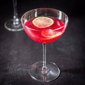 Square photo of the pomegranate cocktail with two lime wheels floating