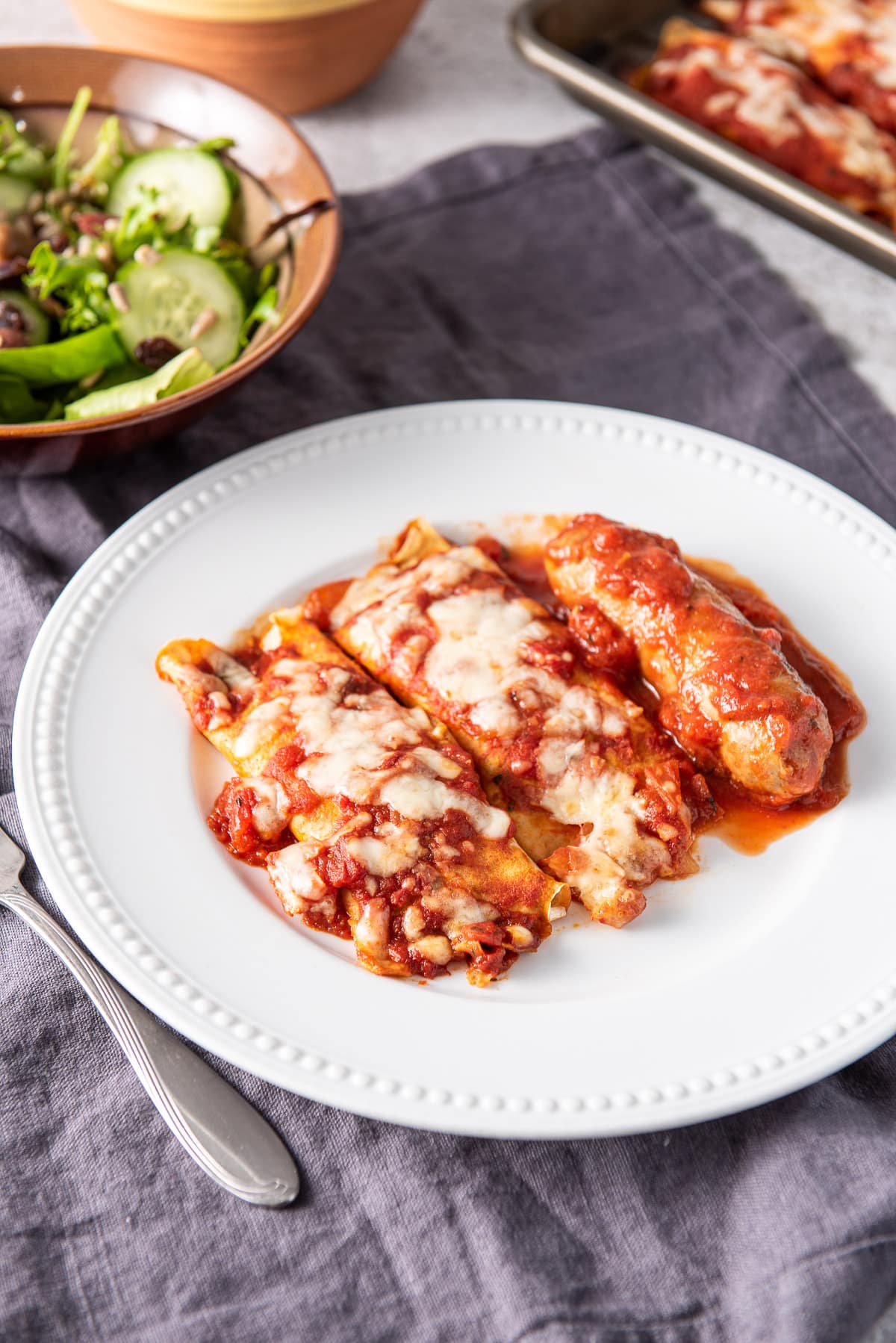 Close up of the baked manicotti and sausage on the beaded white plate