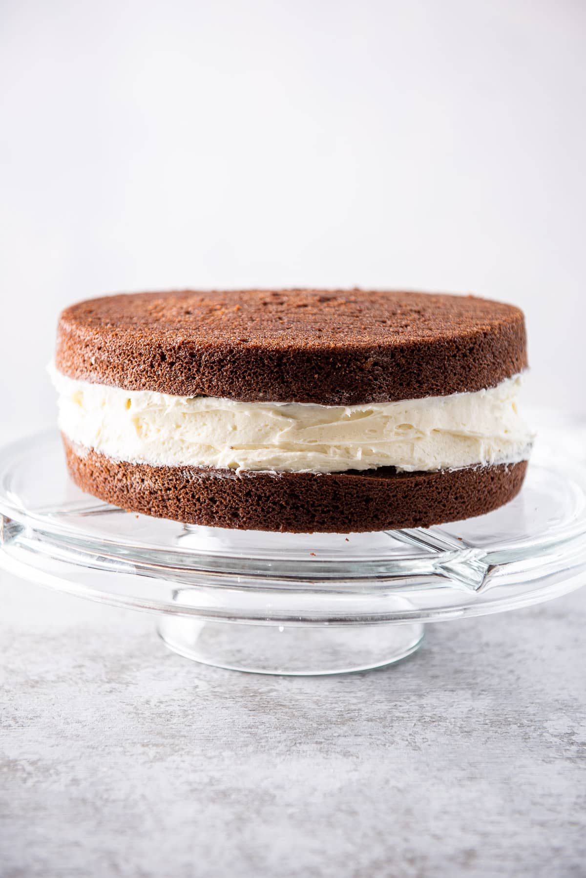 Vertical view of the chocolate cake with a big layer of frosting on a glass pedestal