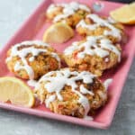 Pink rectangle plate with five crab cakes on it and drizzled with sauce - square