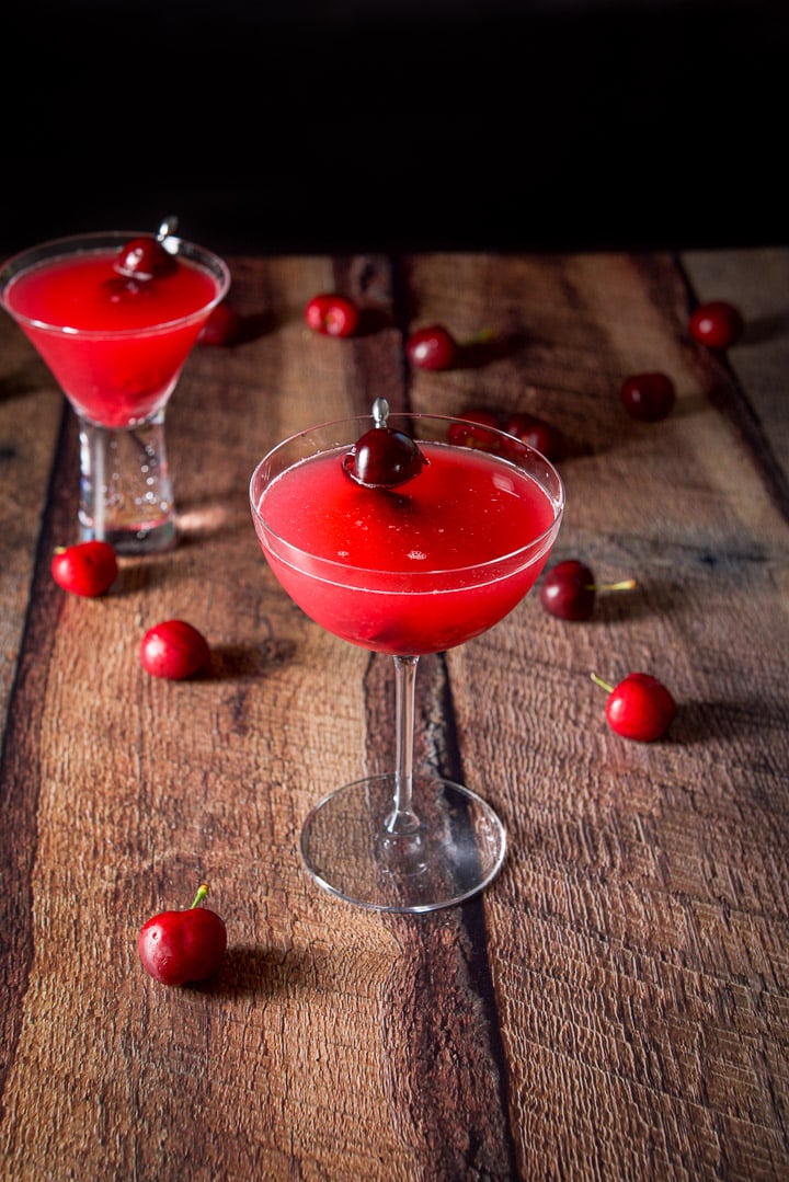 Nearly overhead view of the cosmo with the cherry garnishes in the glasses and cherries on the wooden table