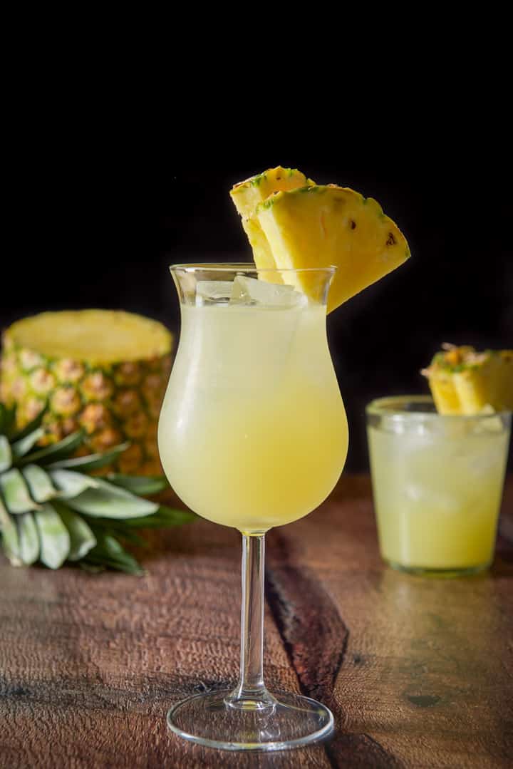 Vertical view of the tulip glass filled with the drink with some pineapple slices on the side of the glass