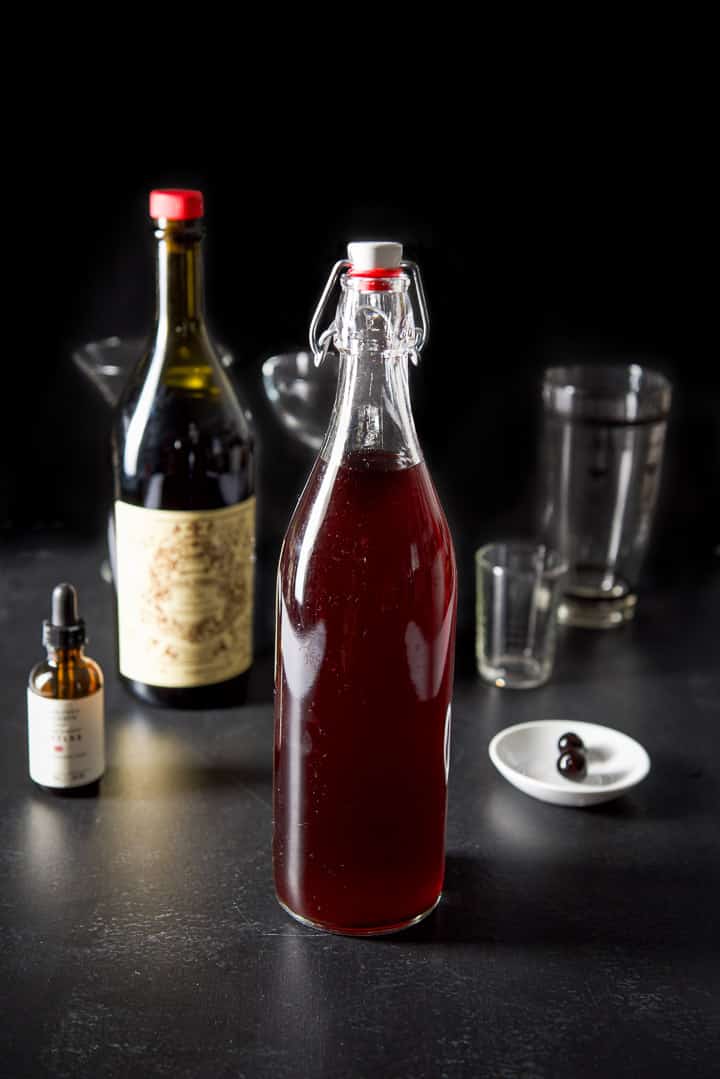 Cherry bourbon, sweet vermouth, cherry bitters and two cherries on a black table