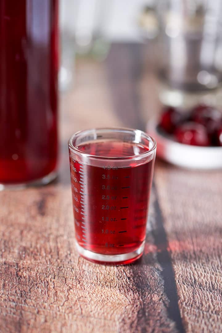 Cherry vodka measured out with the bottle in the background along with some cherries on a little white dish