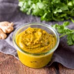 A short glass jar filled with curry paste with cilantro and ginger in the background
