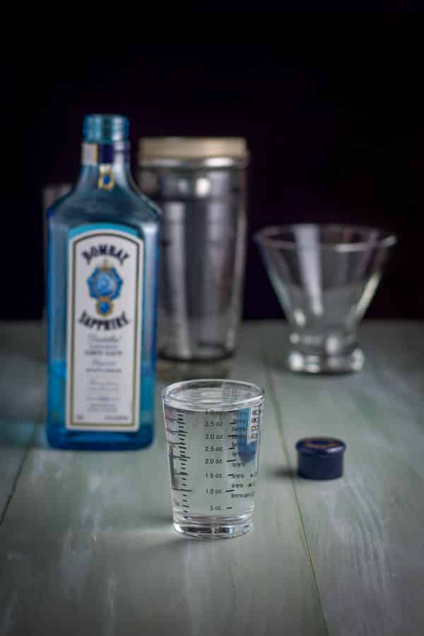 Gin measured with the bottle, glassware and shaker in the background