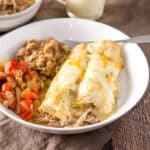 A white bowl with enchiladas with a cream sauce and beans and vegetable - square
