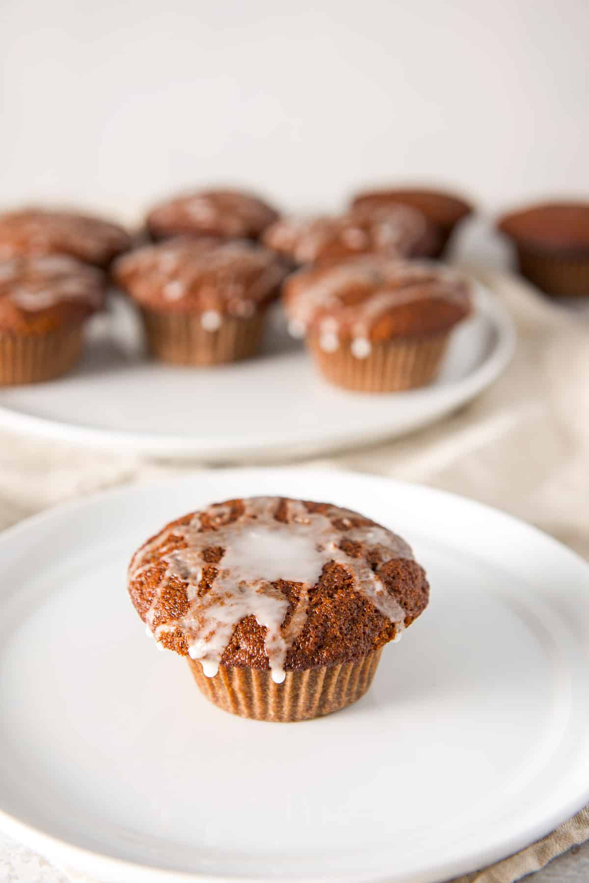 A glazed muffin on a white plate with more in the background