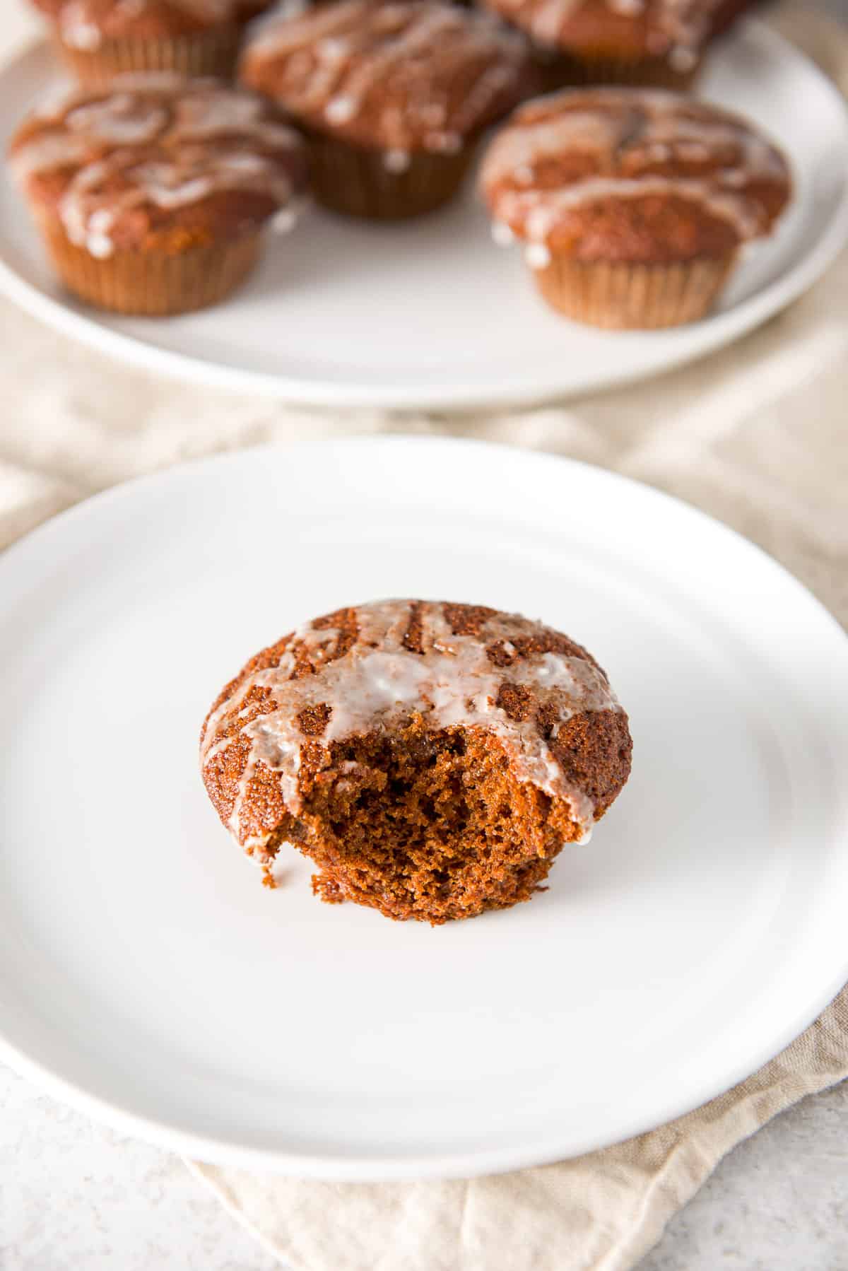 A white plate with a bite out of the glazed muffin and more in the background