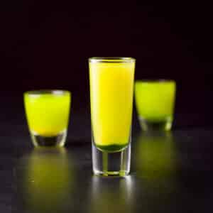 Vertical view of the tall glass filled with the layered shot with the other two glasses in the back - square